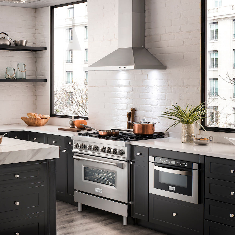 ZLINE Kitchen stainless steel range, range hood, and microwave drawer installed in luxury apartment kitchen with black cabinets and white counters.