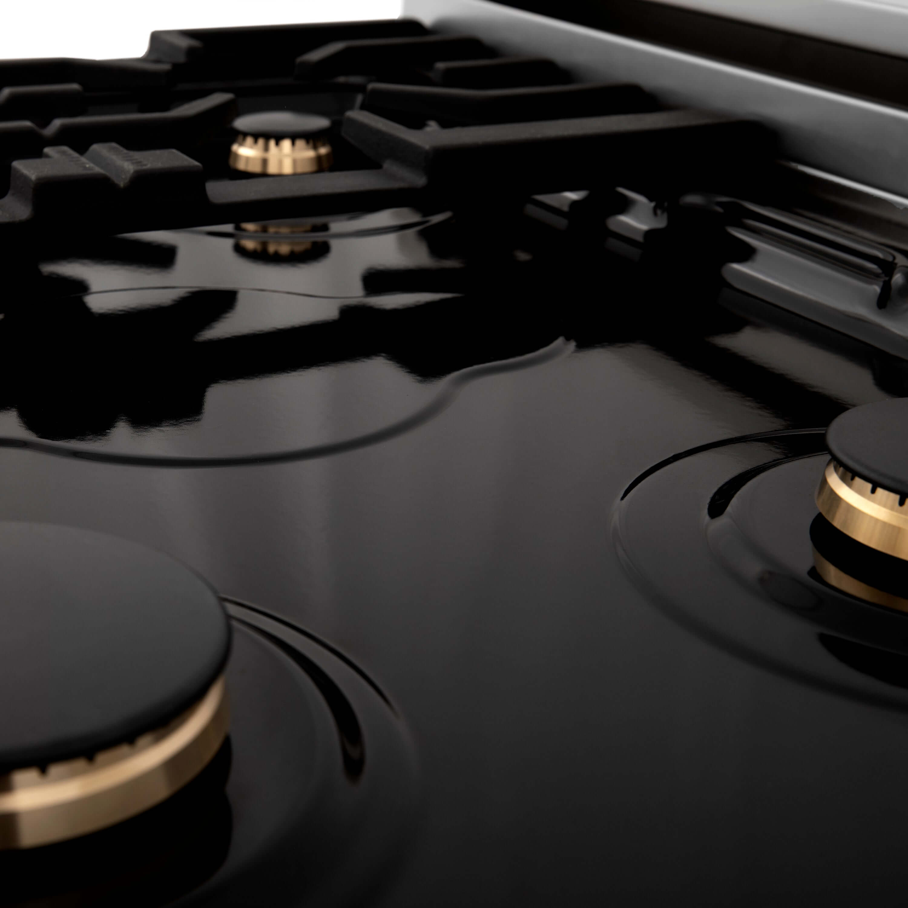 Three ZLINE brass burners on black porcelain cooktop without grates.