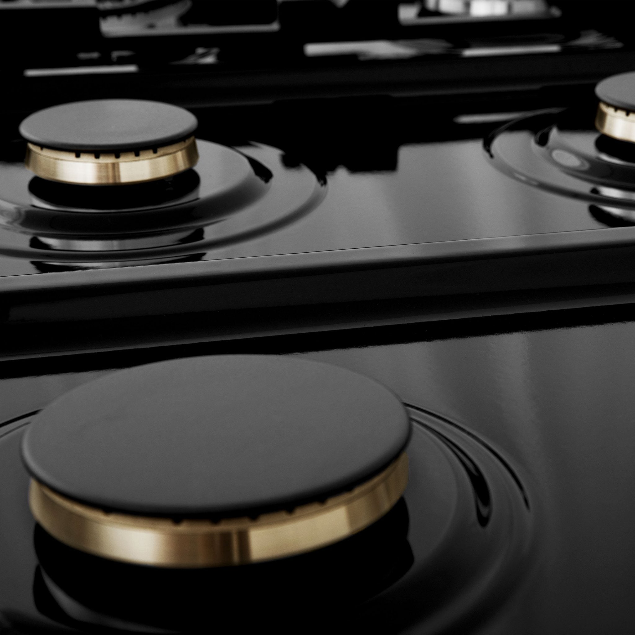 Brass burners on black porcelain cooktop with no grates.