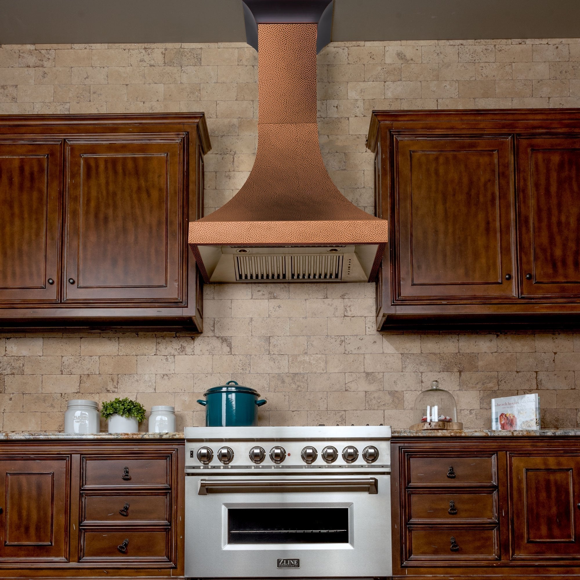 ZLINE Designer Series Hand-Hammered Copper Wall Mount Range Hood in a rustic kitchen with brown cabinets front.