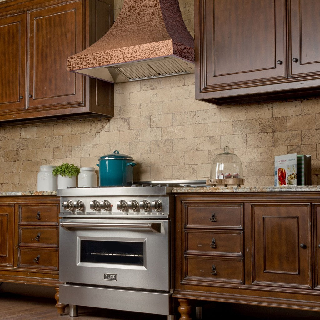 ZLINE Designer Series Hand-Hammered Copper Wall Mount Range Hood in a rustic kitchen with brown cabinets side.