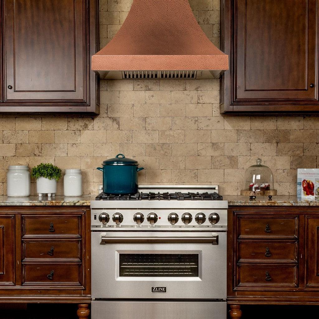 ZLINE Designer Series Hand-Hammered Copper Wall Mount Range Hood in a rustic kitchen with brown cabinets front.