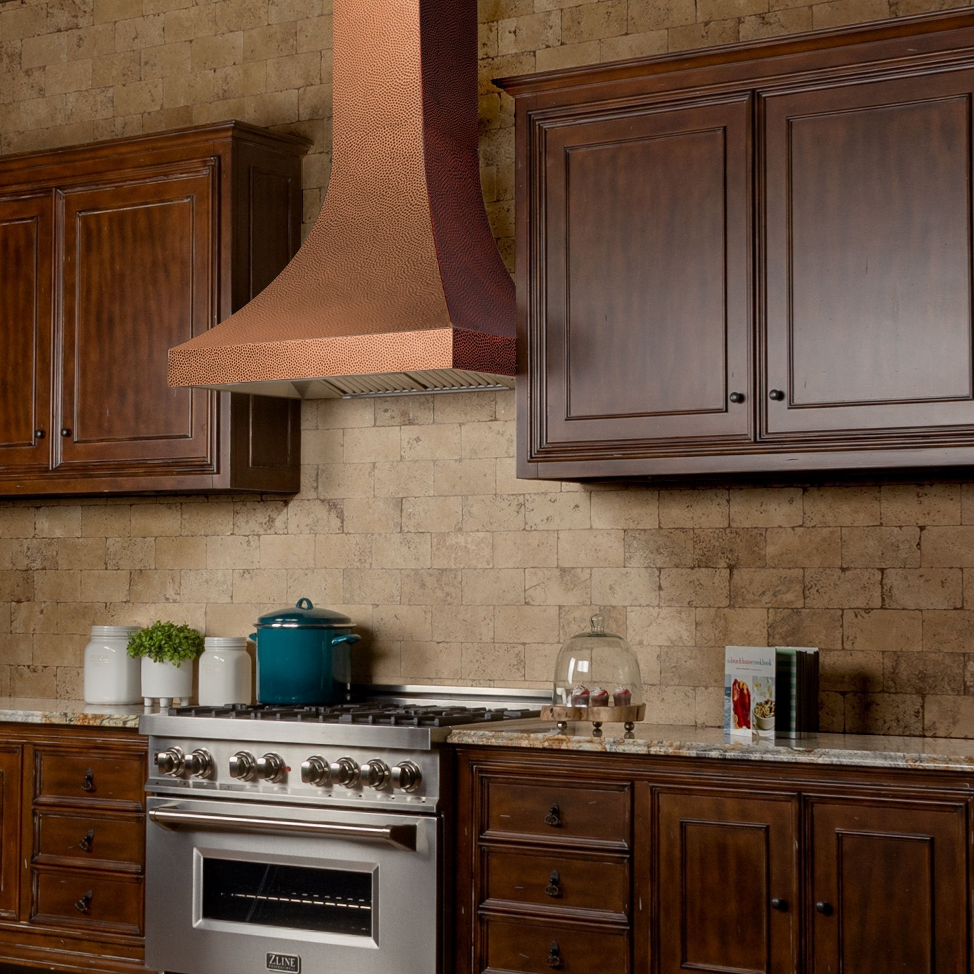 ZLINE Designer Series Hand-Hammered Copper Wall Mount Range Hood in a rustic kitchen with brown cabinets side.