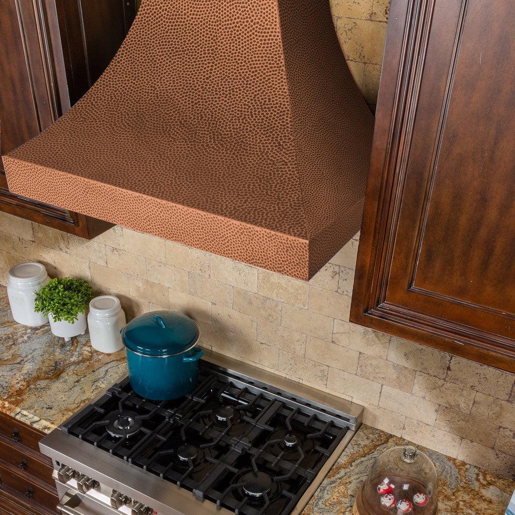 ZLINE Designer Series Hand-Hammered Copper Wall Mount Range Hood in a rustic kitchen with brown cabinets from above.