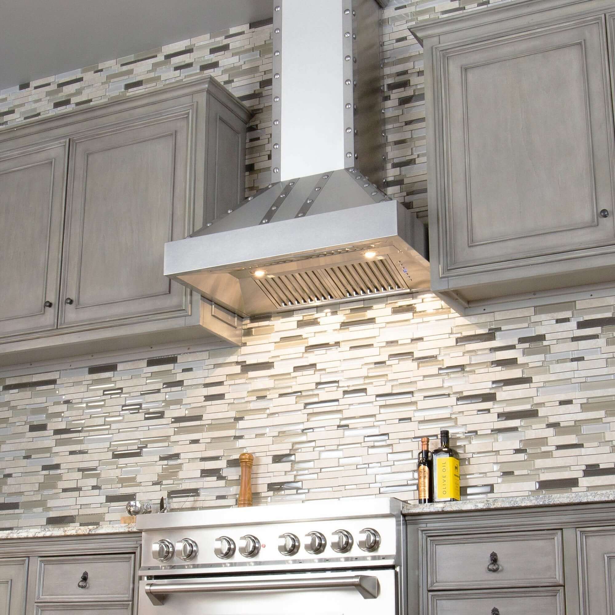 ZLINE Designer Series Wall Mount Range Hood in DuraSnow Stainless Steel with Nailhead Rivets (655-4SSSS) in a modern luxury kitchen with LED lighting activated.