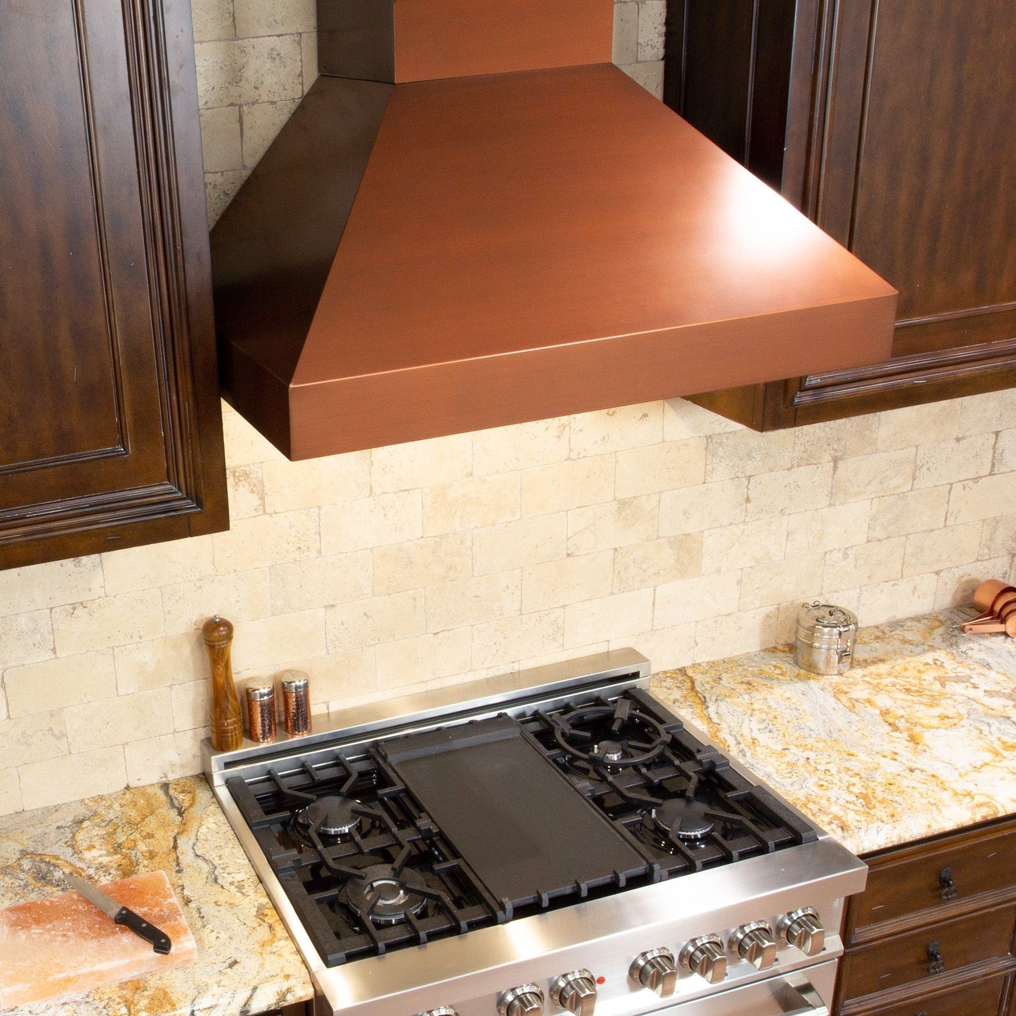 ZLINE Convertible Designer Series Copper Wall Mount Range Hood (8667C) in a rustic-style kitchen with brown cabinets from above with cooktop lighting on.